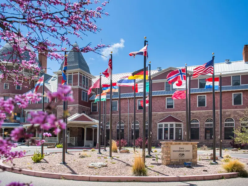 The Davis International Center, formerly Montezuma Castle, with flags in front and a redbud tree in bloom