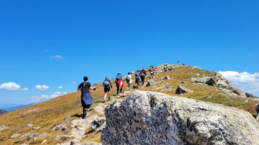 A line of students hiking up a rocky mountain ridge under a blue sky